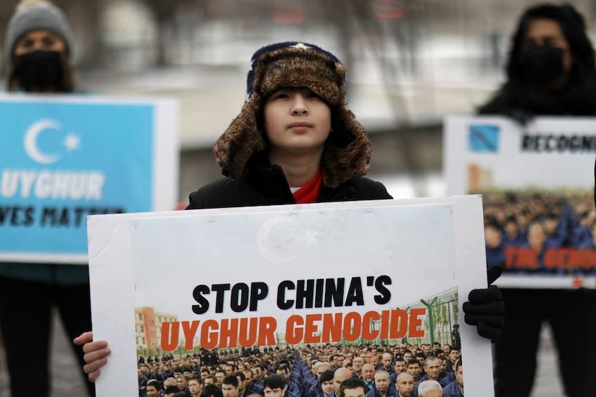 A young boy in a furry hat holds a poster 'Stop China's Uighur genocide' 
