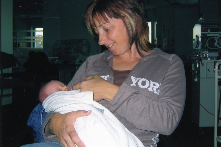 A woman holds a young baby wrapped inside a blanket.