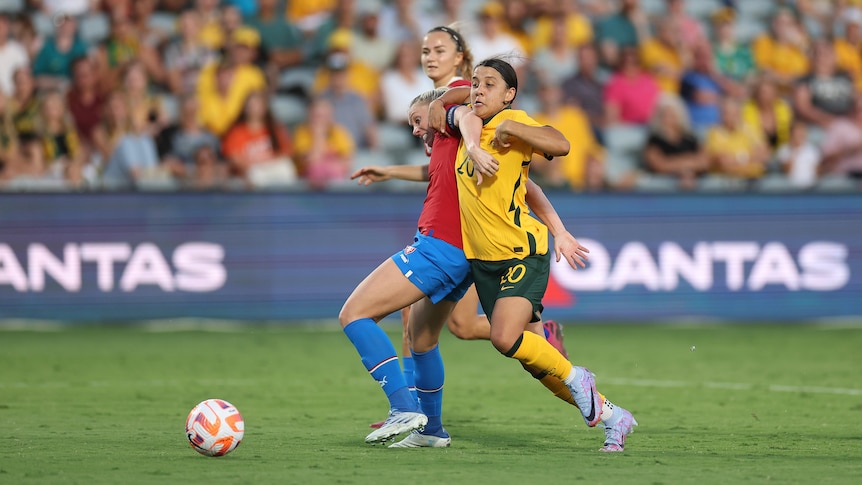 A soccer player wearing yellow and green wrestles with a player wearing red and blue during a game