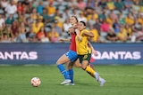 A soccer player wearing yellow and green wrestles with a player wearing red and blue during a game
