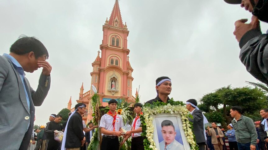 Men stand with a portrait of the deceased outside a church.
