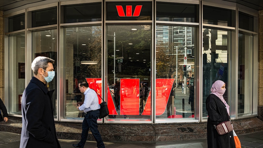 People in masks walk past a Westpac building in a city.