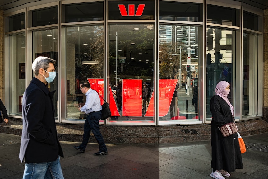 People in masks walk past a Westpac building in a city.