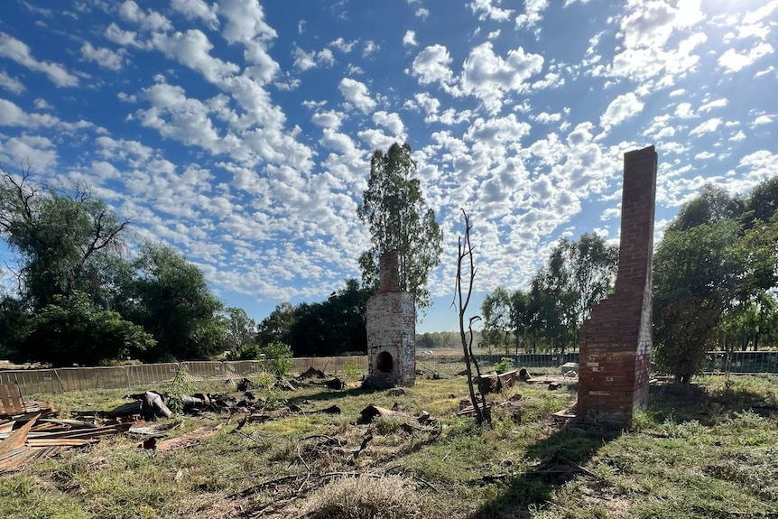 An old fireplace and chimney stack stand in a field against a blue and cloudy sky