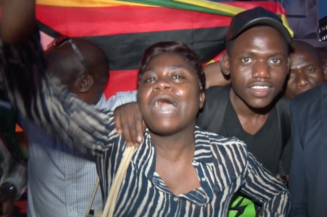 People cheer and hold a Zimbabwe flag.