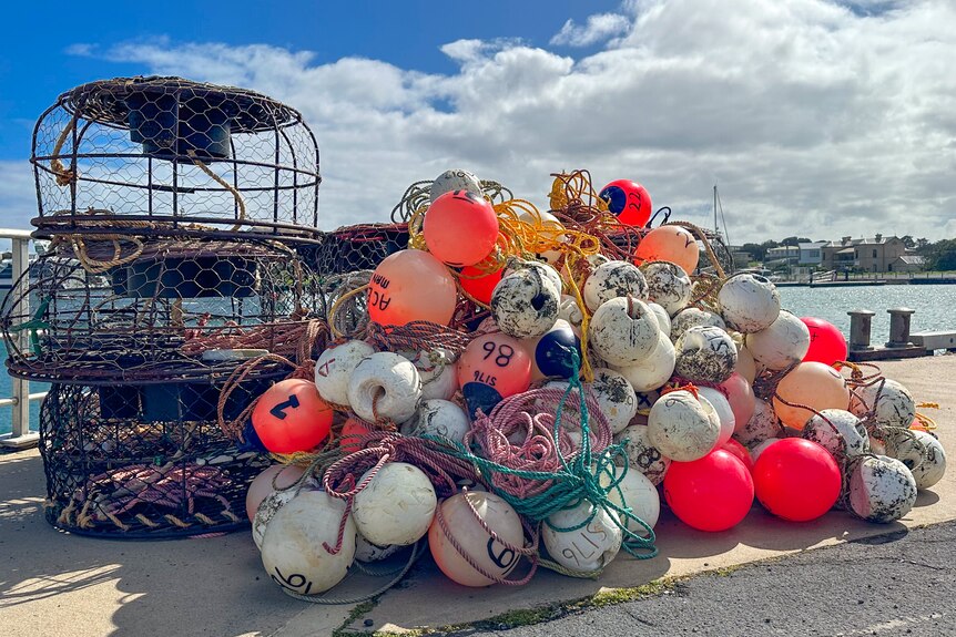 Three lobster pots stacked up beside a pile of buoys on a wharf.