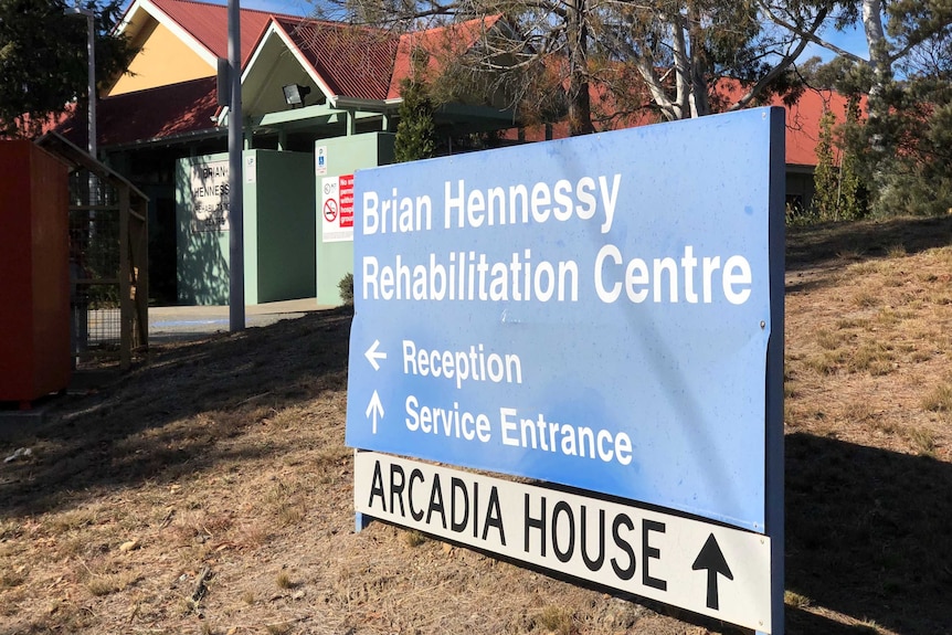 A bent sign sits outside the entrance to the Brian Hennessy rehabilitation centre on a sunny day.