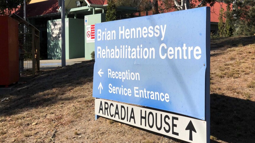 A bent sign sits outside the entrance to the Brian Hennessy rehabilitation centre on a sunny day.