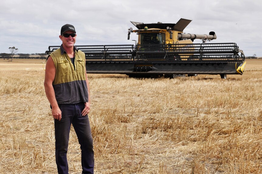 Man standing in paddock with header behind him.