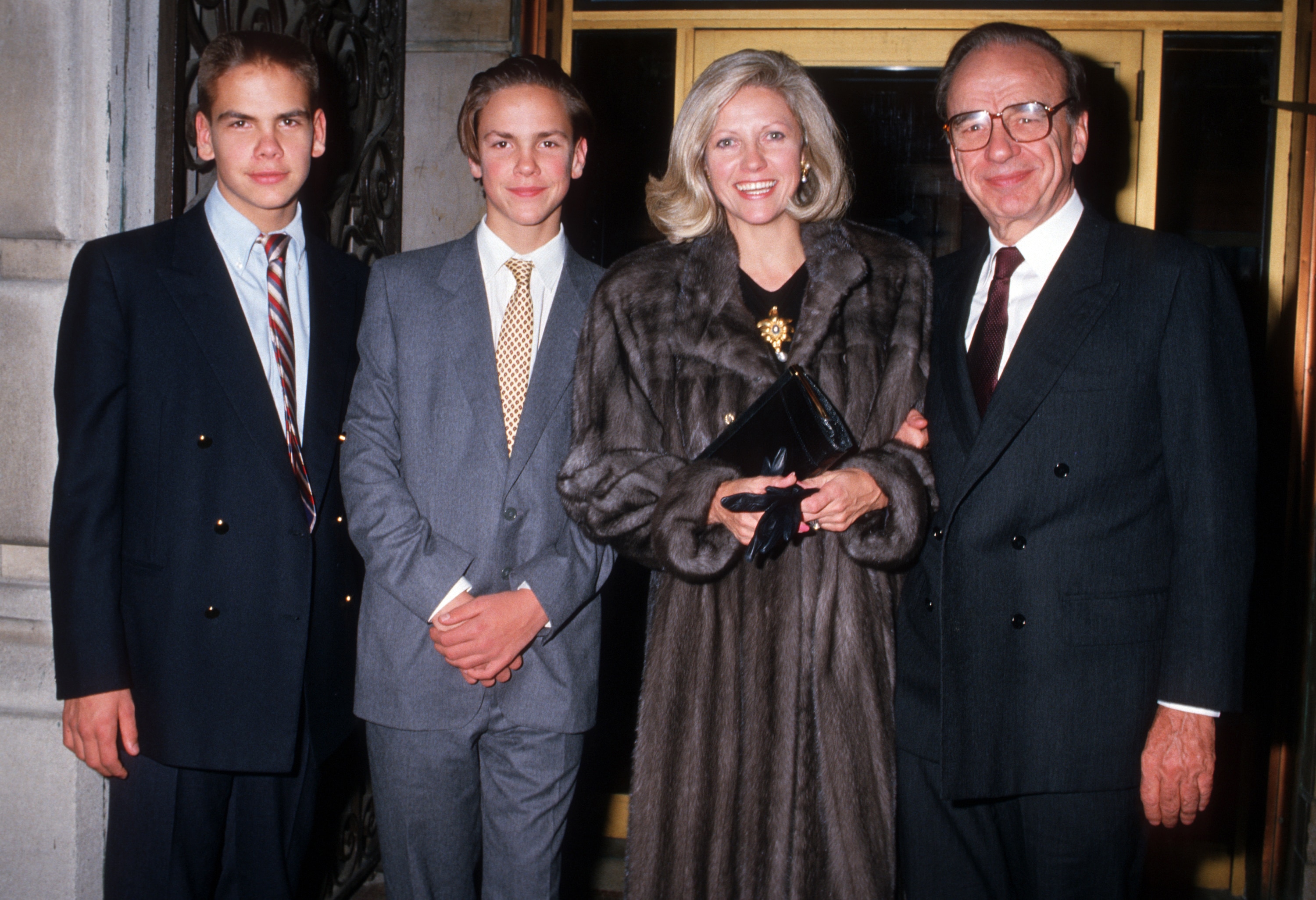 A woman in a fur coat, and three men in suits pose for a photo