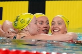 three australian swimmers give each other a hug over the lane rope, all are wearing yellow swimming caps