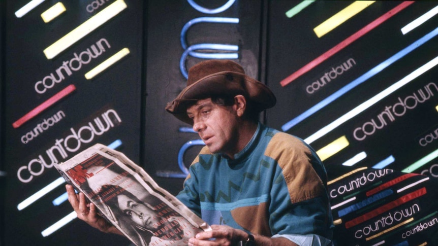 Male wearing a cowboy hat sitting down reading a magazine.