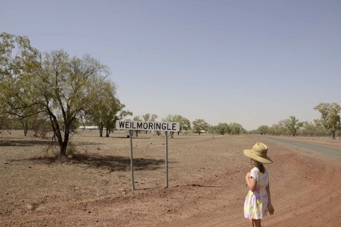 A photo of a girl in a hat looking at a dry drought landscape and a sign that says "Weilmoringle"