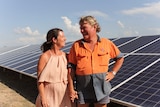 Lyn and Doug Scouller looking at each other and smiling. They stand in front of a row of solar panels.