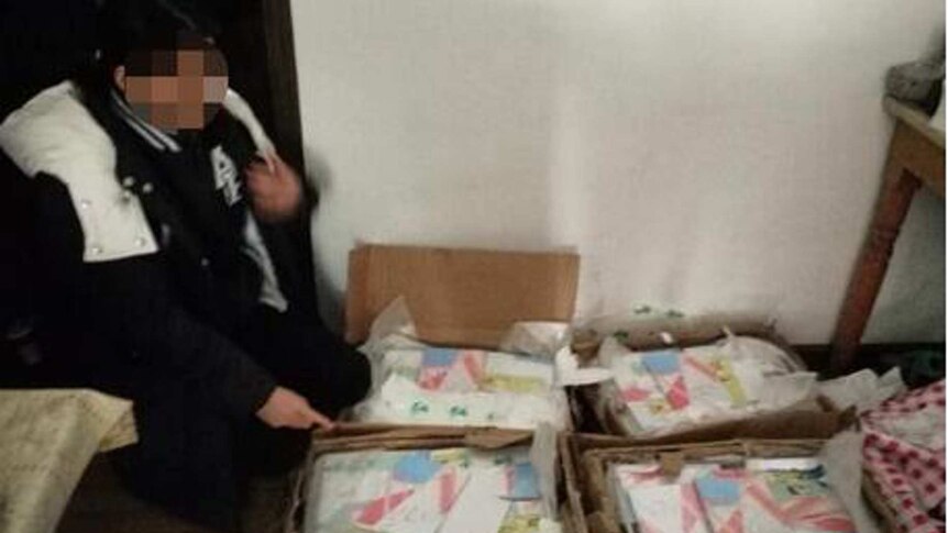 A person with a blurred face stands near boxes full of the book Occupied, which is illegal in China.