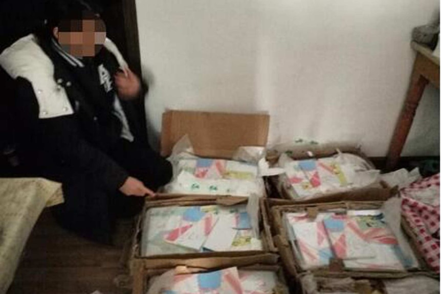 A person with a blurred face stands near boxes full of the book Occupied, which is illegal in China.