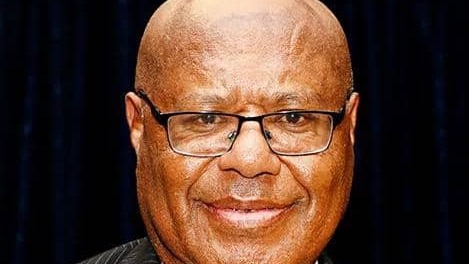 Headshot of a bald black man wearing glasses, suit and tie