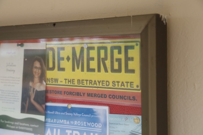 A sign in the style of a license plate reads "De-merge, NSW- the betrayed state, restore forcibly merged councils"