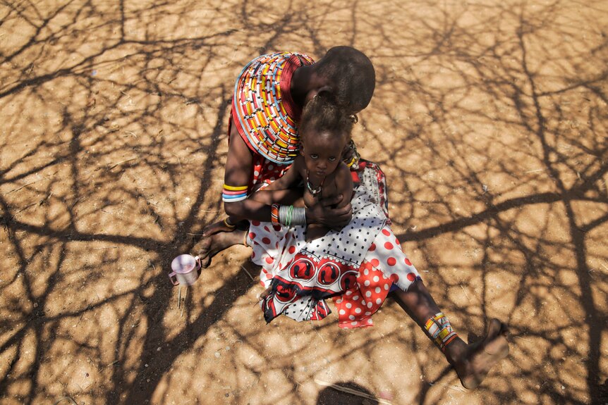 a woman cradles her young child on the dry dirt
