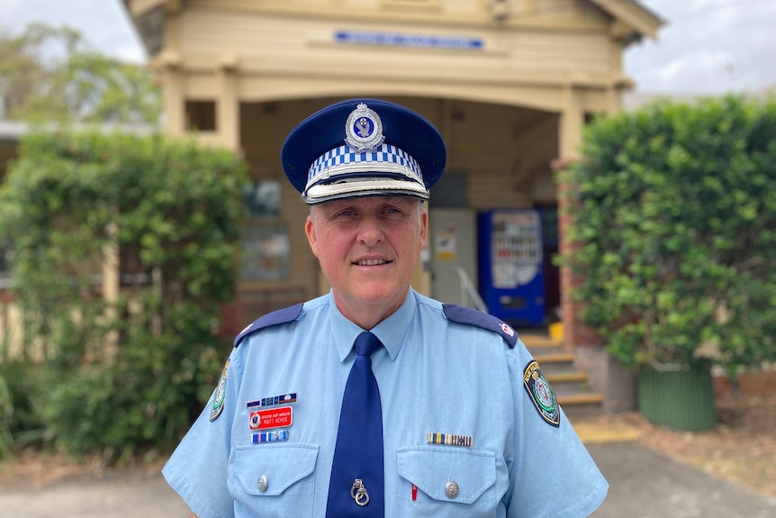 A police officer in a hat stands in front of Byron Bay Station.