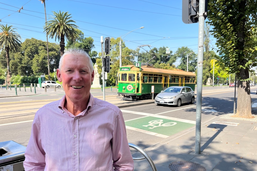 Man in pink shirt stands on street smiling at camera