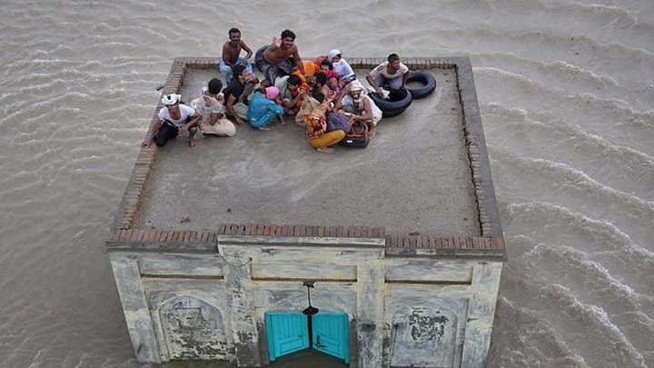 picture of people stranded on a roof due to the flood water on the grond