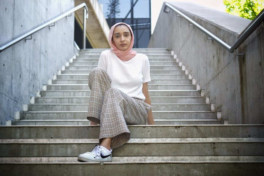 Woman in pink headscarf and white t-shirt sits on cement steps.