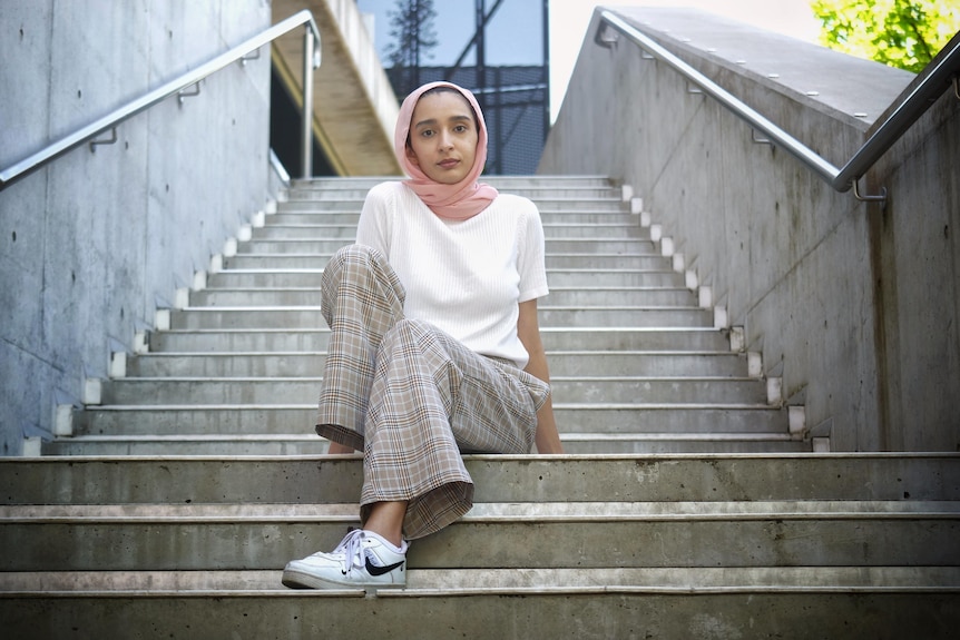 Woman in pink headscarf and white t-shirt sits on cement steps.