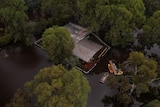 A house surrounded by water and trees with a canoe with materials on it