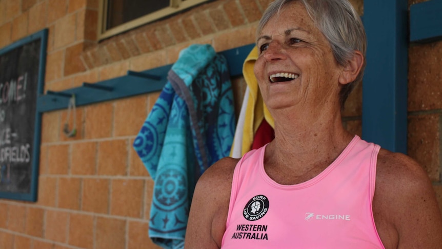 She stands near towels hanging against bricks and laughs