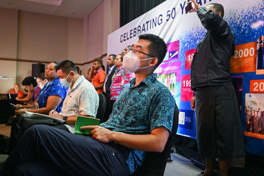 A row of people watching an address with a Chinese delegate in the foreground.