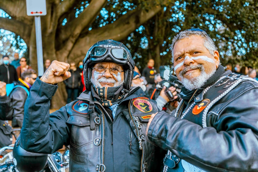 Two men smiling, with white markings on their face and Aboriginal biker jackets.