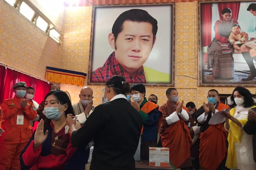 A woman wearing a face mask is surrounded by monks and receives an injection