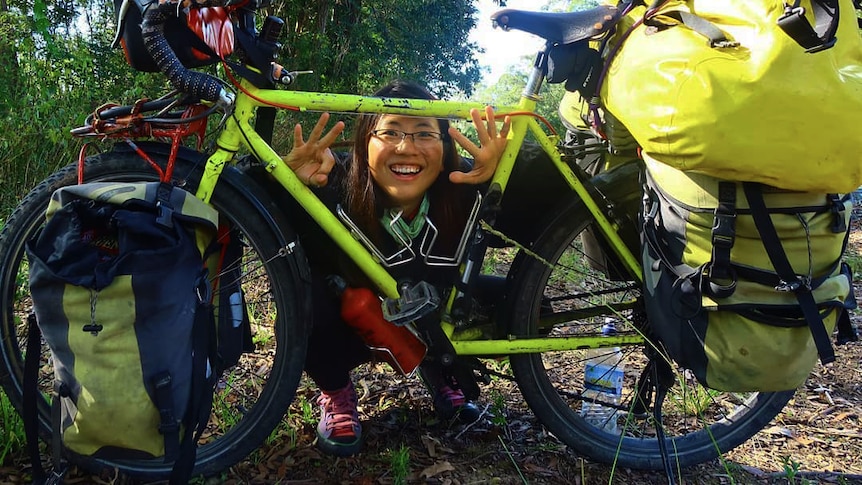 A woman squats down and grins through the frame of a bright green bicycle.