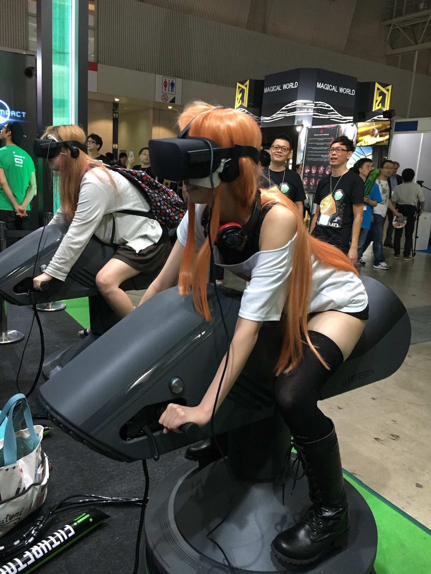 Two women have a turn at a virtual reality motorbike game