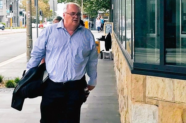 A man with a blue shirt carrying a jacket and documents.