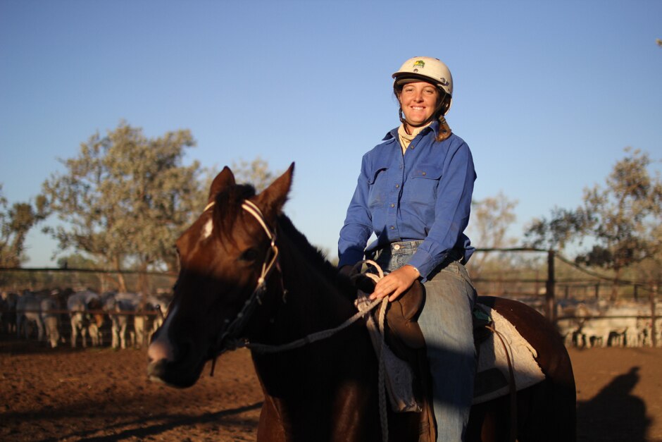 A woman in a white hard hat riding a brown horse.