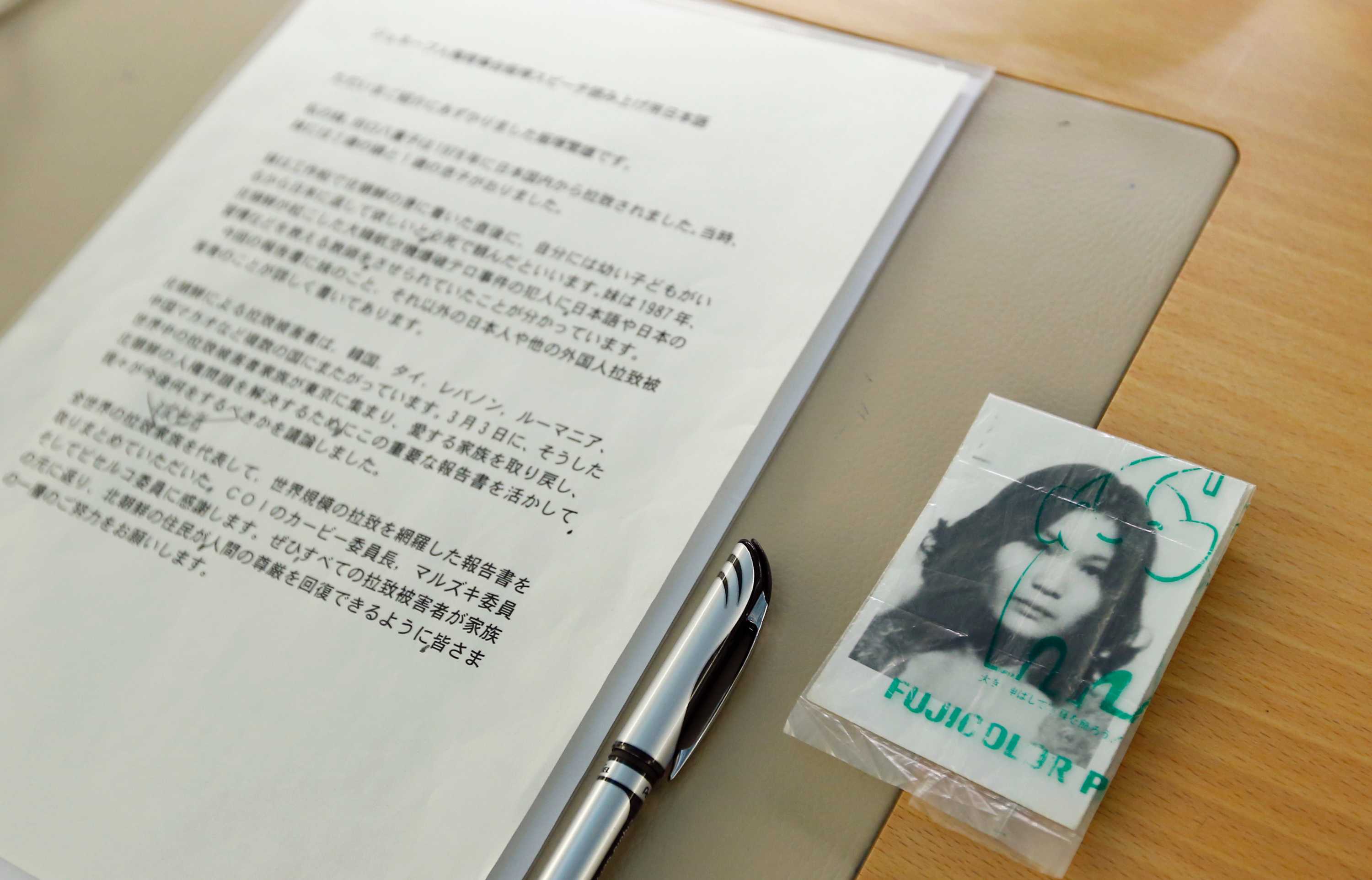 A black and white passport-style photo of a young Asian woman sits inside a plastic sleeve next to an A4 Japanese document.