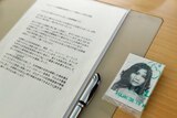 A black and white passport-style photo of a young Asian woman sits inside a plastic sleeve next to an A4 Japanese document.