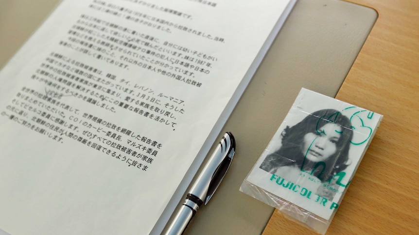 A black and white passport-style photo of a young Asian woman sits inside a plastic sleeve next to an A4 Japanese document.