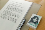 A black and white passport-style photo of a young Asian woman sits inside a plastic sleeve next to an A4 Japanese document.