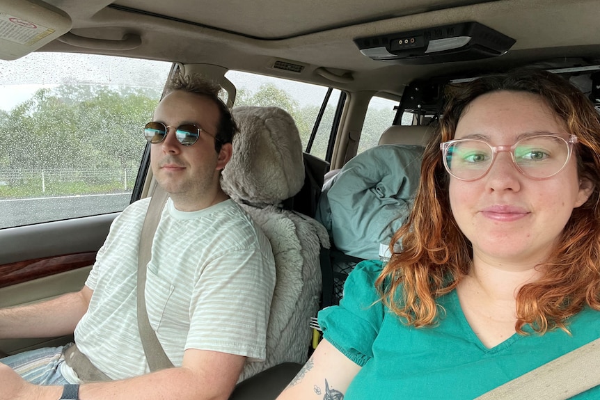 Woman in green top and glasses in car next to man in sunglasses and white t-shirt.