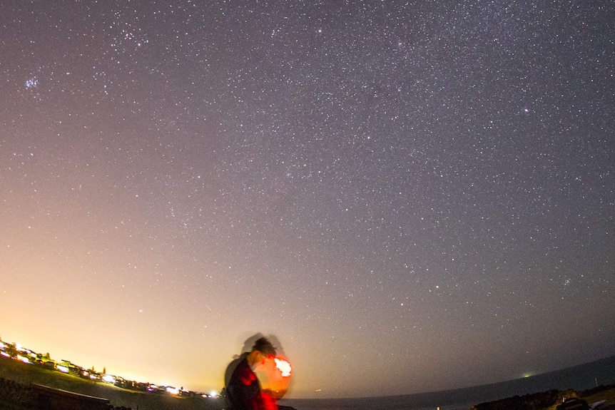 Chris Dengate looks at his phone standing under the night sky filled with stars