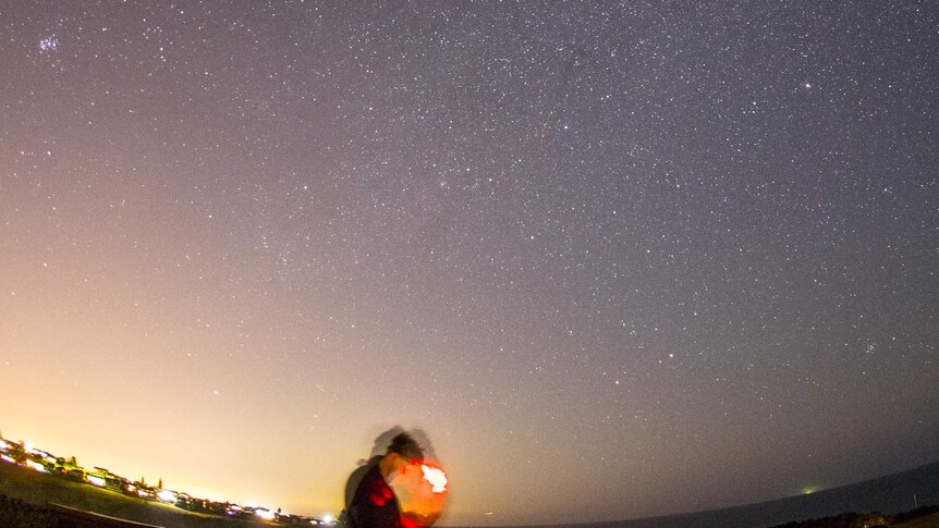 Chris Dengate looks at his phone standing under the night sky filled with stars