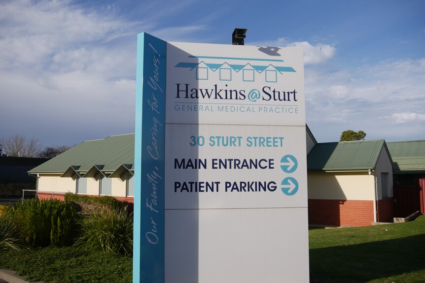 A billboard stands in front of neat bricked rows of medical suites, with a blue sky in the background