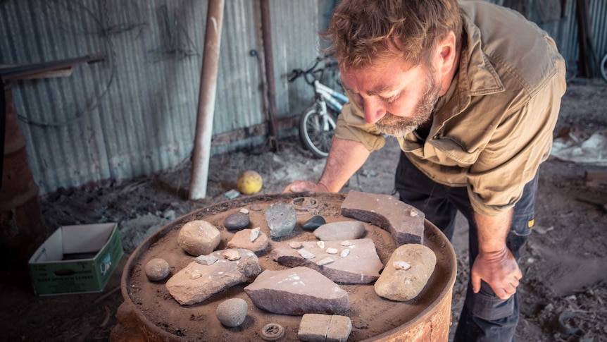 John Martin bends down to look at a group of small stone objects.