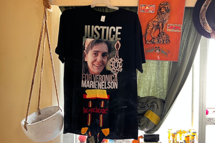 A T-shirt hangs from a windowsill inside a home. It has a picture of a woman and reads "Justice for Veronica Marie Nelson"