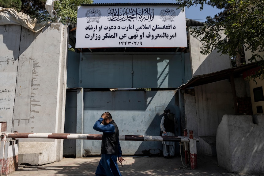 A man walks past a white banner with black writing, hung on the front of a building. 