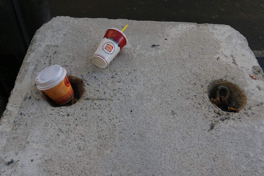 Empty cups and cigarette butts sit atop a concrete bollard outside Southern Cross Station in Melbourne.