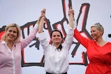 Three women hold their hands in the air smiling.
